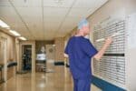 Medical professional writing on a dry wipe board in a hospital corridor.